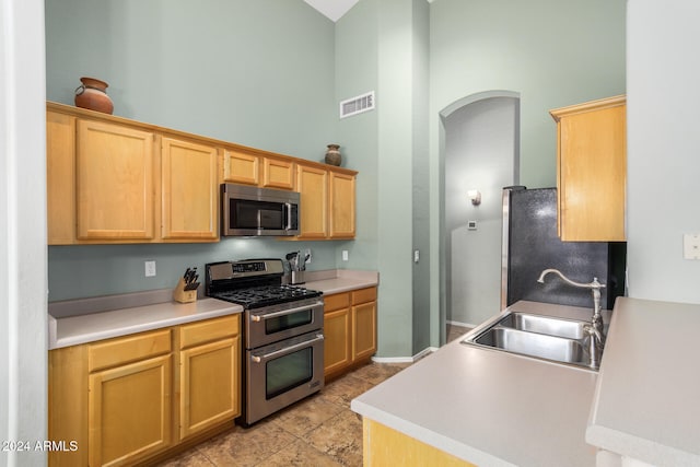 kitchen featuring appliances with stainless steel finishes, sink, light tile patterned floors, and a towering ceiling