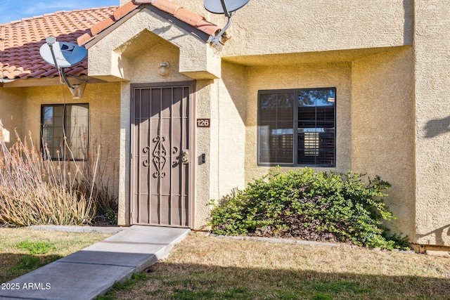 view of exterior entry with a tiled roof and stucco siding