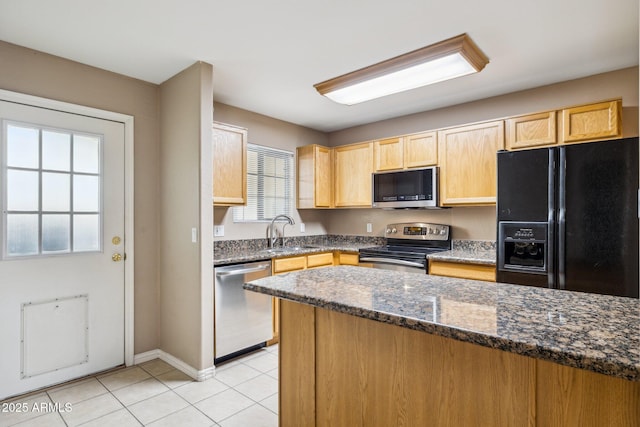 kitchen with light tile patterned floors, dark stone countertops, stainless steel appliances, light brown cabinetry, and a sink