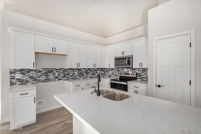 kitchen with light hardwood / wood-style floors, white cabinets, vaulted ceiling, stainless steel appliances, and backsplash