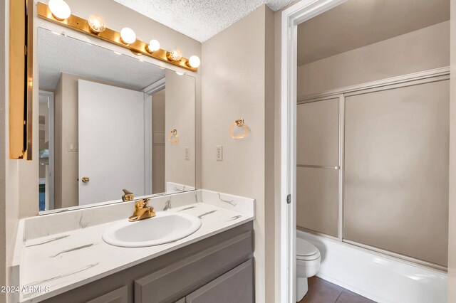 full bathroom featuring tile patterned flooring, a textured ceiling, shower / bath combination with glass door, vanity, and toilet