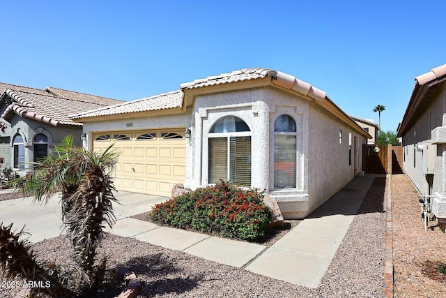 mediterranean / spanish home featuring concrete driveway, stucco siding, fence, a tiled roof, and a garage