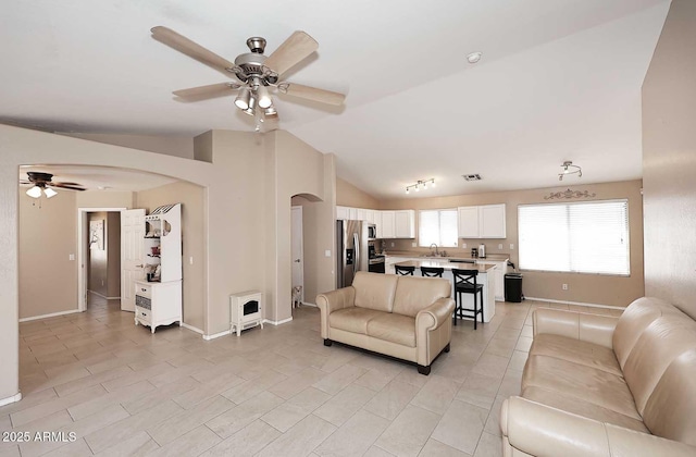 living room with arched walkways, ceiling fan, baseboards, and vaulted ceiling