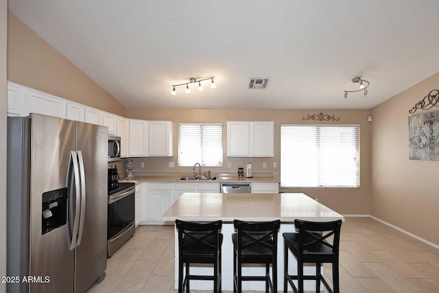 kitchen with light countertops, a sink, a kitchen breakfast bar, stainless steel appliances, and visible vents