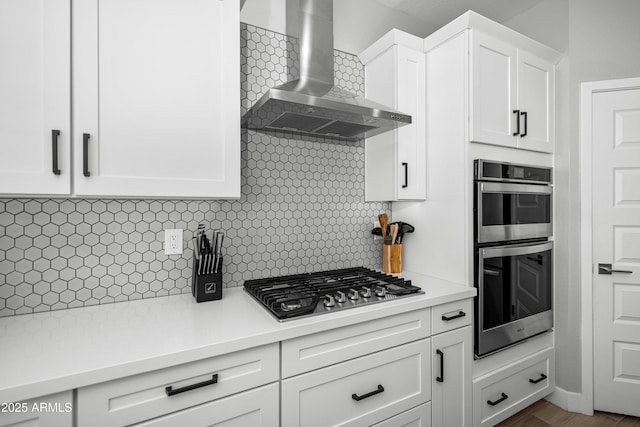 kitchen featuring tasteful backsplash, wall chimney range hood, stainless steel appliances, and white cabinets