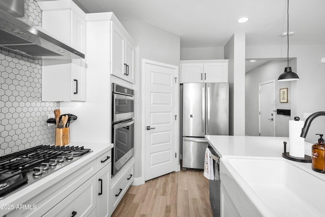 kitchen with appliances with stainless steel finishes, pendant lighting, white cabinetry, decorative backsplash, and wall chimney exhaust hood