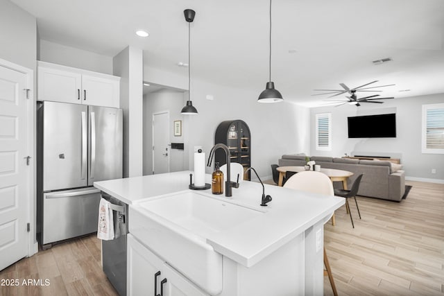 kitchen with pendant lighting, sink, white cabinets, stainless steel appliances, and a center island with sink