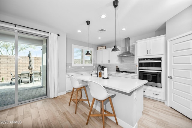 kitchen with wall chimney exhaust hood, decorative light fixtures, a center island with sink, appliances with stainless steel finishes, and white cabinets