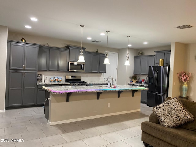 kitchen with visible vents, decorative backsplash, light stone countertops, a kitchen breakfast bar, and appliances with stainless steel finishes