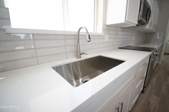 kitchen with white cabinets, decorative backsplash, light stone counters, appliances with stainless steel finishes, and a sink