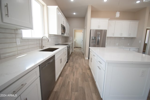 kitchen with a center island, stainless steel appliances, light wood-style flooring, white cabinetry, and a sink