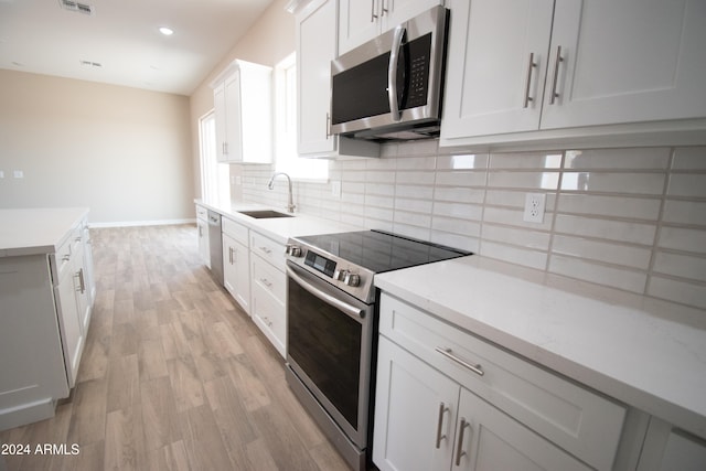 kitchen featuring light wood finished floors, stainless steel appliances, decorative backsplash, white cabinets, and a sink