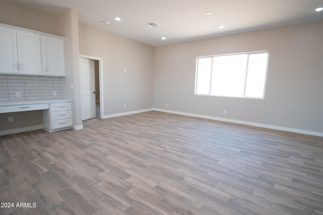 interior space featuring light wood finished floors, baseboards, built in desk, and recessed lighting