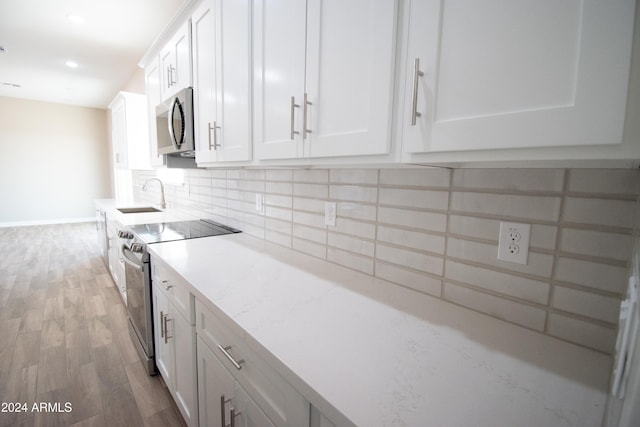 kitchen with a sink, white cabinets, appliances with stainless steel finishes, light wood finished floors, and tasteful backsplash