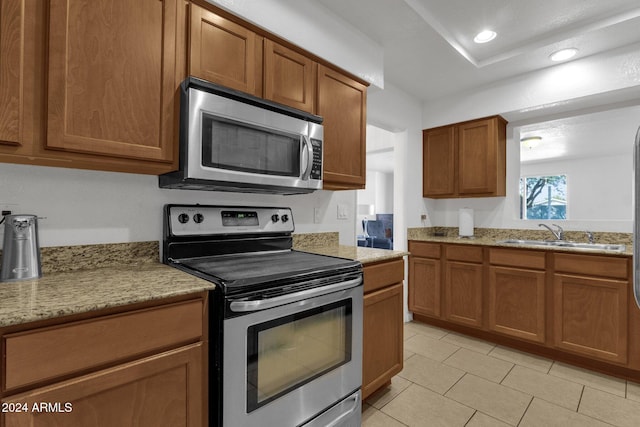 kitchen with appliances with stainless steel finishes, light tile patterned floors, light stone counters, and sink