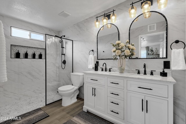 bathroom with wood-type flooring, a textured ceiling, tiled shower, vanity, and tile walls