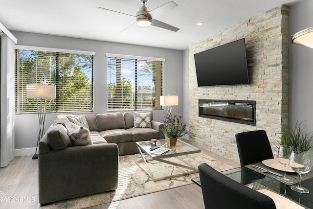 living room featuring a stone fireplace, light hardwood / wood-style floors, and ceiling fan