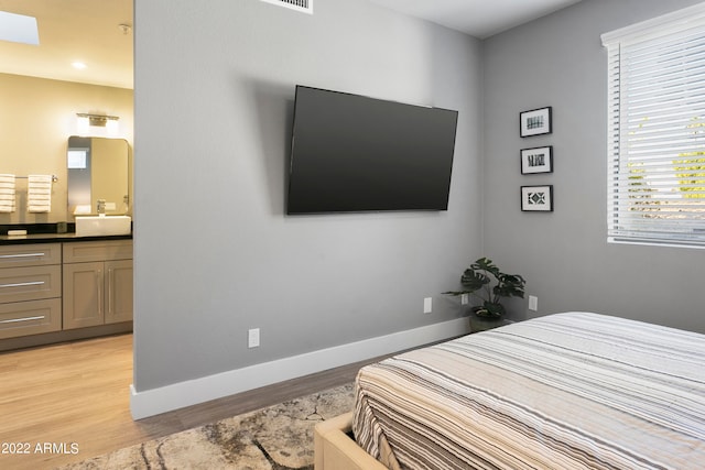 bedroom with sink, ensuite bathroom, and light wood-type flooring