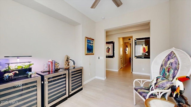 sitting room with ceiling fan, wine cooler, and light wood-type flooring