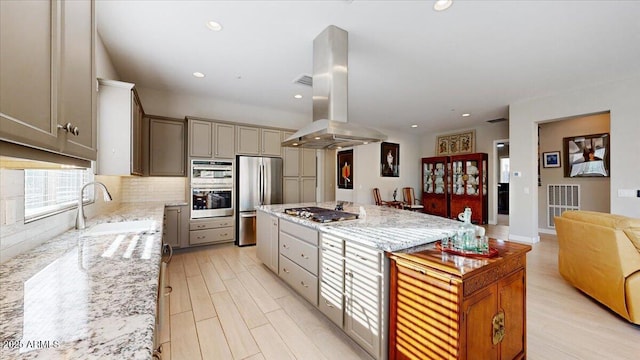 kitchen with appliances with stainless steel finishes, sink, decorative backsplash, island exhaust hood, and light stone counters