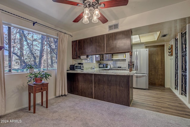 kitchen featuring ceiling fan, stainless steel fridge, light wood-type flooring, dark brown cabinets, and kitchen peninsula