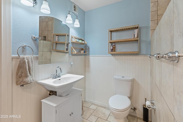 bathroom featuring tile patterned floors, visible vents, toilet, a sink, and wainscoting