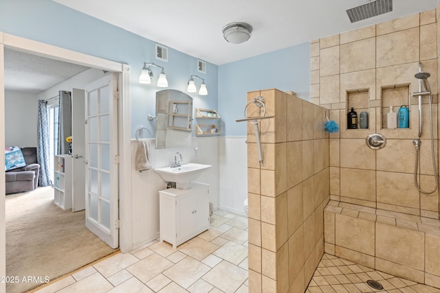 full bath featuring a sink, visible vents, tiled shower, and wainscoting