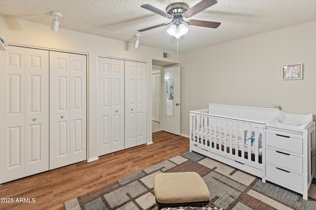 bedroom featuring wood finished floors, visible vents, a crib, multiple closets, and a textured ceiling