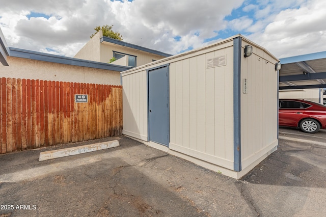 view of shed with covered parking and fence