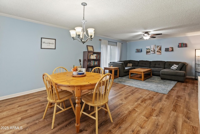 dining space with a textured ceiling, wood finished floors, ceiling fan with notable chandelier, and ornamental molding