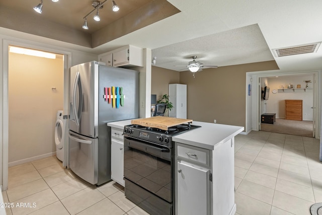 kitchen featuring visible vents, light countertops, freestanding refrigerator, black range with gas cooktop, and separate washer and dryer