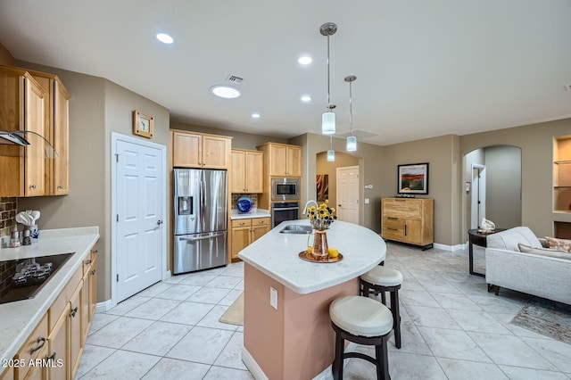 kitchen with arched walkways, stainless steel appliances, open floor plan, a kitchen island with sink, and a kitchen breakfast bar