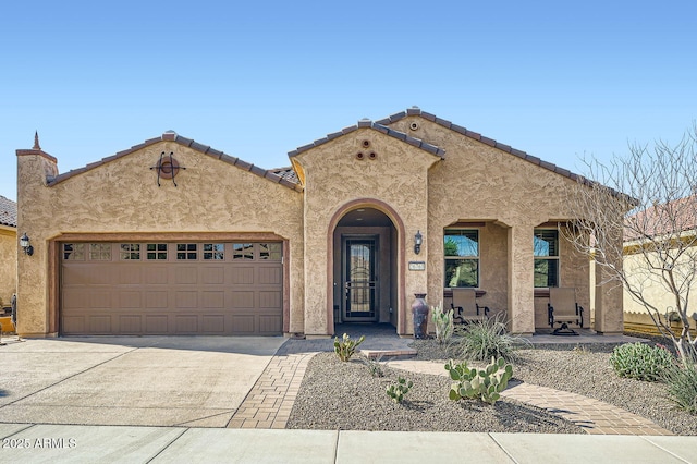 mediterranean / spanish-style home with a garage, driveway, a tiled roof, and stucco siding