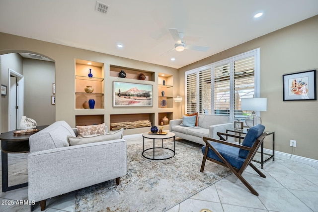 living room with baseboards, visible vents, arched walkways, a ceiling fan, and built in shelves