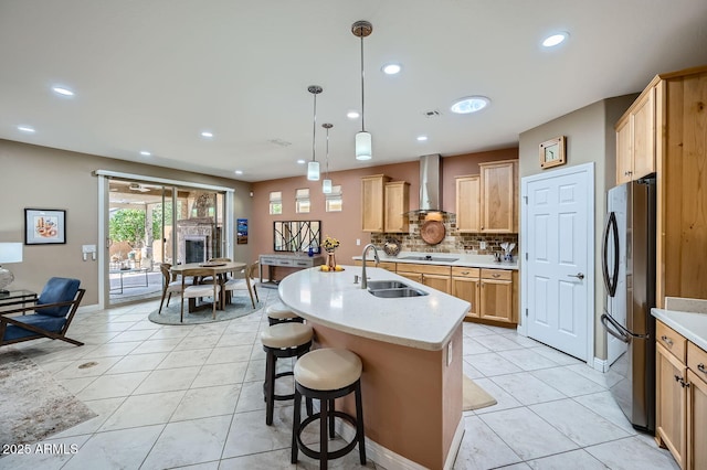 kitchen featuring a center island with sink, wall chimney exhaust hood, freestanding refrigerator, pendant lighting, and a sink