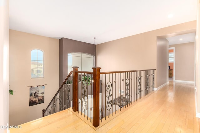 corridor featuring baseboards, hardwood / wood-style floors, and an upstairs landing