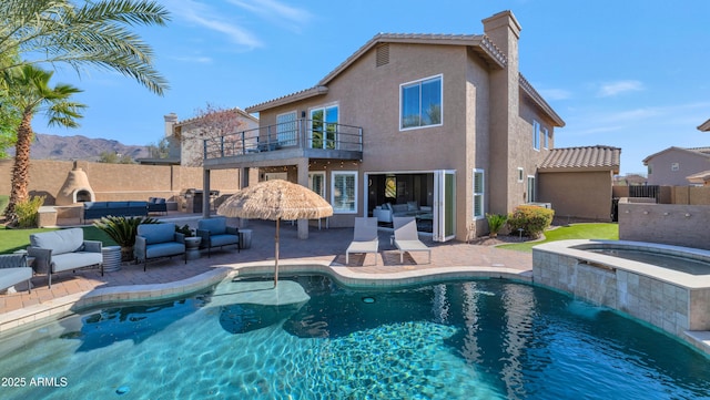 rear view of house featuring a patio, a balcony, a pool with hot tub, an outdoor living space, and a mountain view