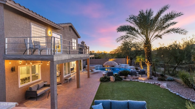 yard at dusk featuring a balcony, an outdoor hangout area, a fenced in pool, and a patio