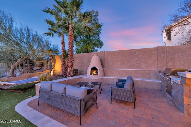 patio terrace at dusk with exterior fireplace, a grill, and an outdoor kitchen