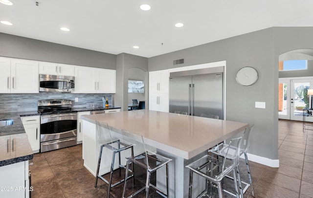 kitchen featuring a breakfast bar, a kitchen island, dark tile patterned floors, stainless steel appliances, and white cabinets