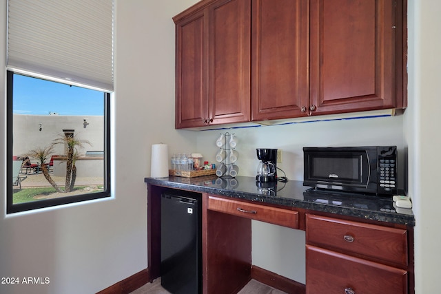 kitchen featuring black appliances, dark stone counters, and built in desk