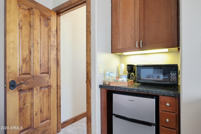 kitchen with light wood-type flooring, stainless steel fridge, and dark stone countertops