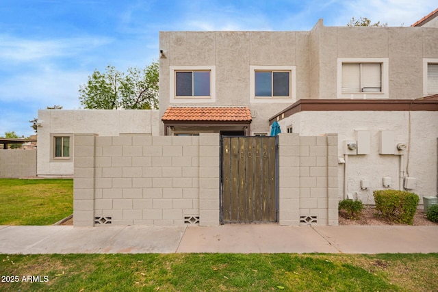 townhome / multi-family property with stucco siding, fence, a front lawn, and a gate