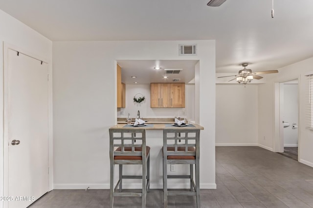 kitchen with baseboards, visible vents, a breakfast bar, ceiling fan, and light countertops