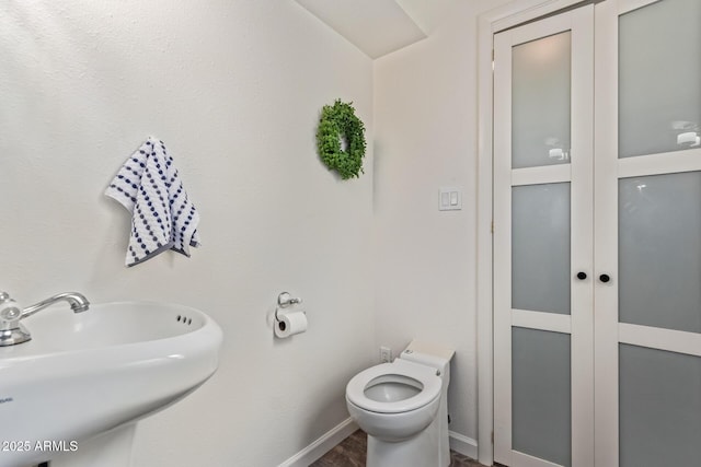 half bath featuring toilet, baseboards, and a sink