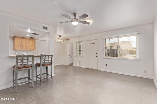 interior space featuring baseboards, a kitchen breakfast bar, visible vents, and ceiling fan