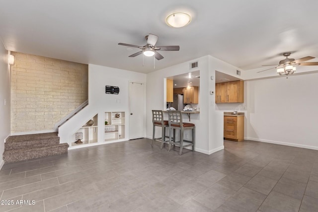 unfurnished living room with stairway, built in shelves, a ceiling fan, visible vents, and baseboards