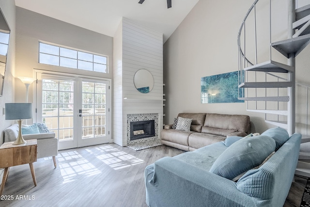 living room featuring french doors, high vaulted ceiling, a tile fireplace, and light hardwood / wood-style flooring