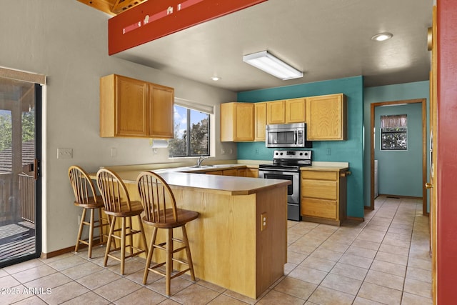 kitchen with appliances with stainless steel finishes, sink, kitchen peninsula, light tile patterned flooring, and a breakfast bar area