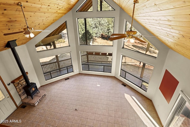 unfurnished living room featuring wood ceiling, ceiling fan, a wood stove, tile patterned flooring, and high vaulted ceiling